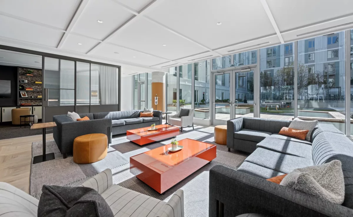 Modern co‑working lounge with sectional seating, tables, and floor‑to‑ceiling windows.