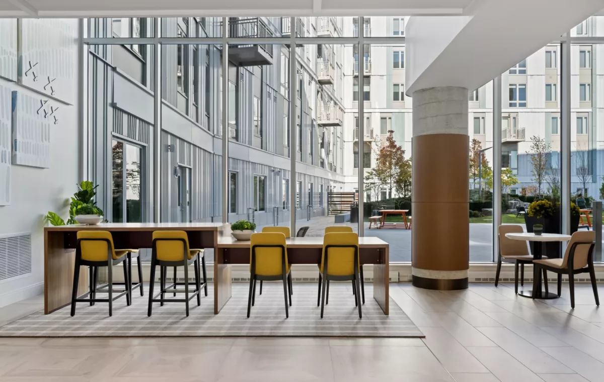 Community dining area with long table, bar seating, and large windows.