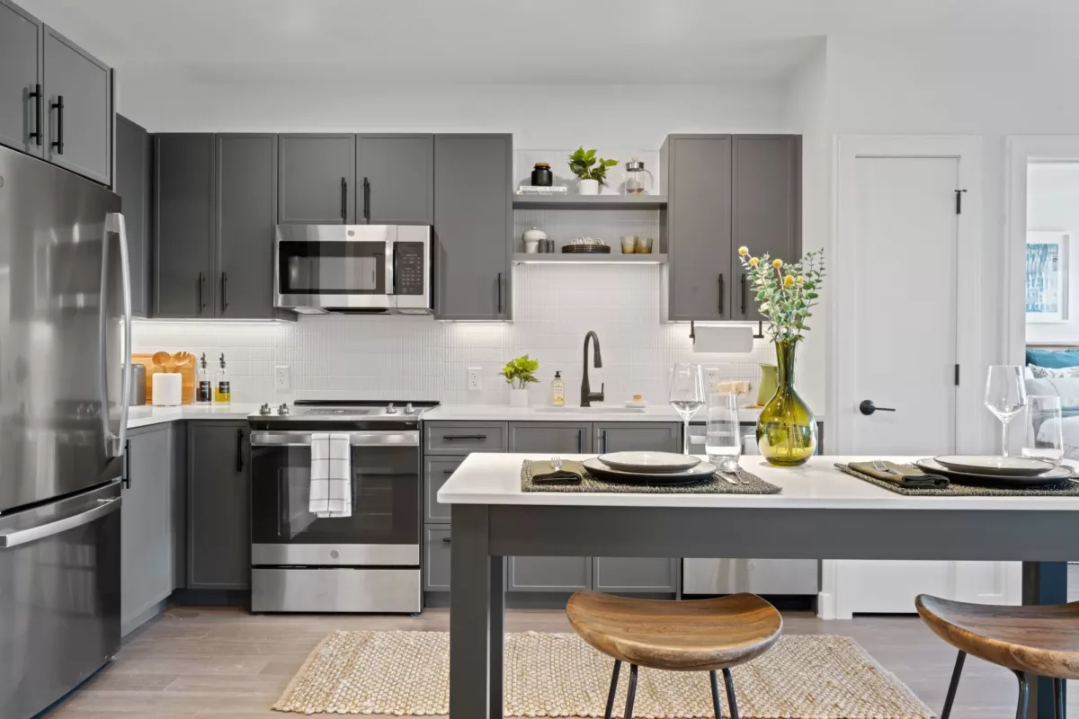 Modern apartment kitchen with stainless steel appliances, gray cabinets, and island seating.