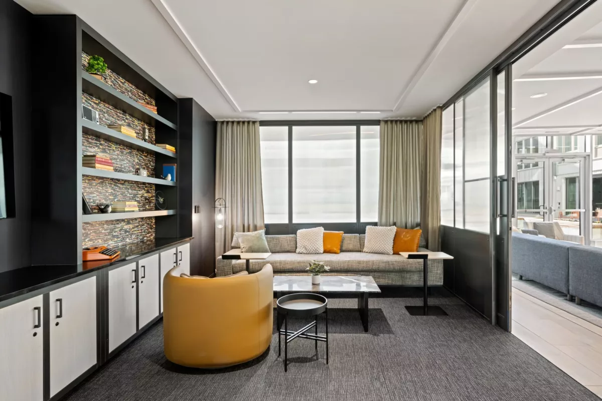 Lounge area with sofa, accent chair, built‑in shelving, and large windows.