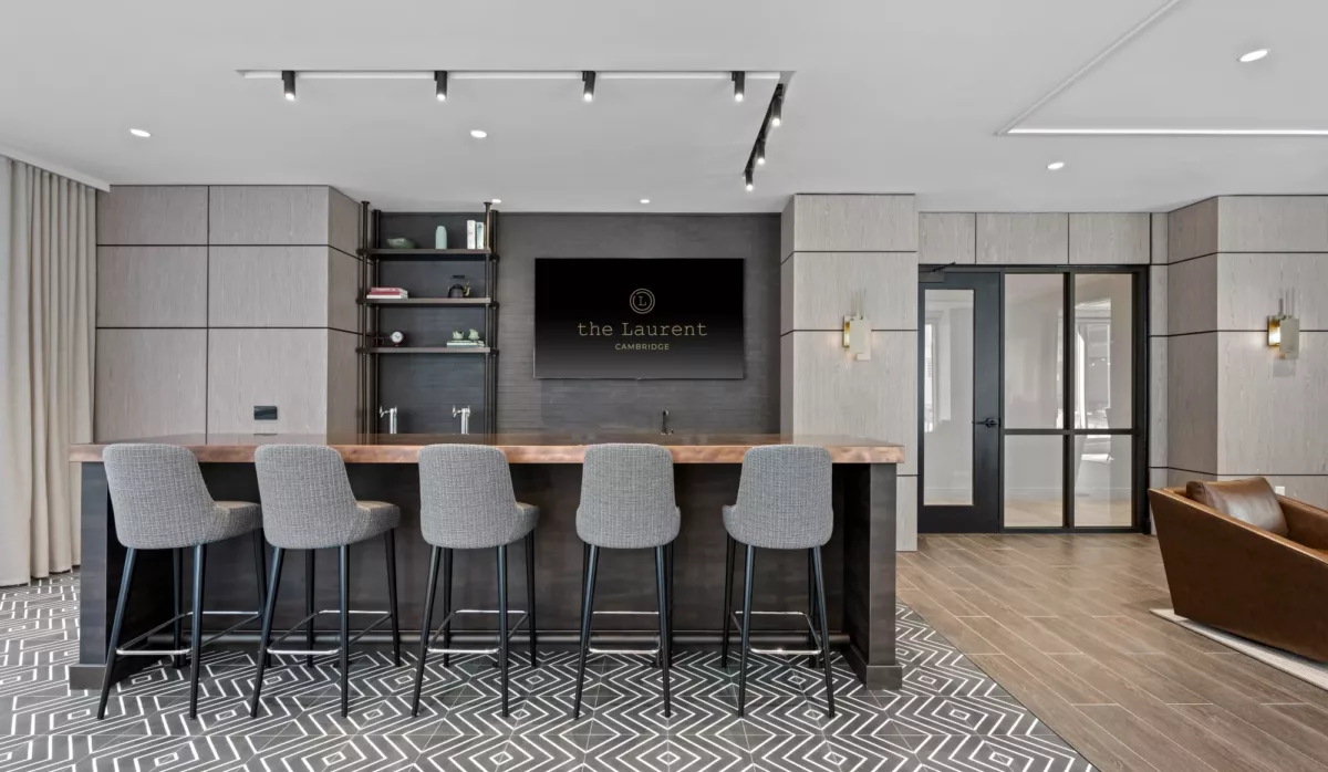 Clubroom kitchen with bar seating, dark cabinetry, and wall‑mounted television.