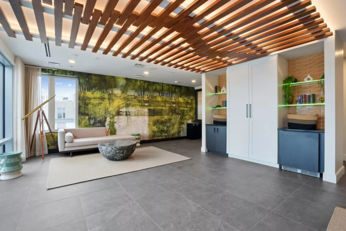Covered outdoor lounge with seating, greenery, and wood slat ceiling.